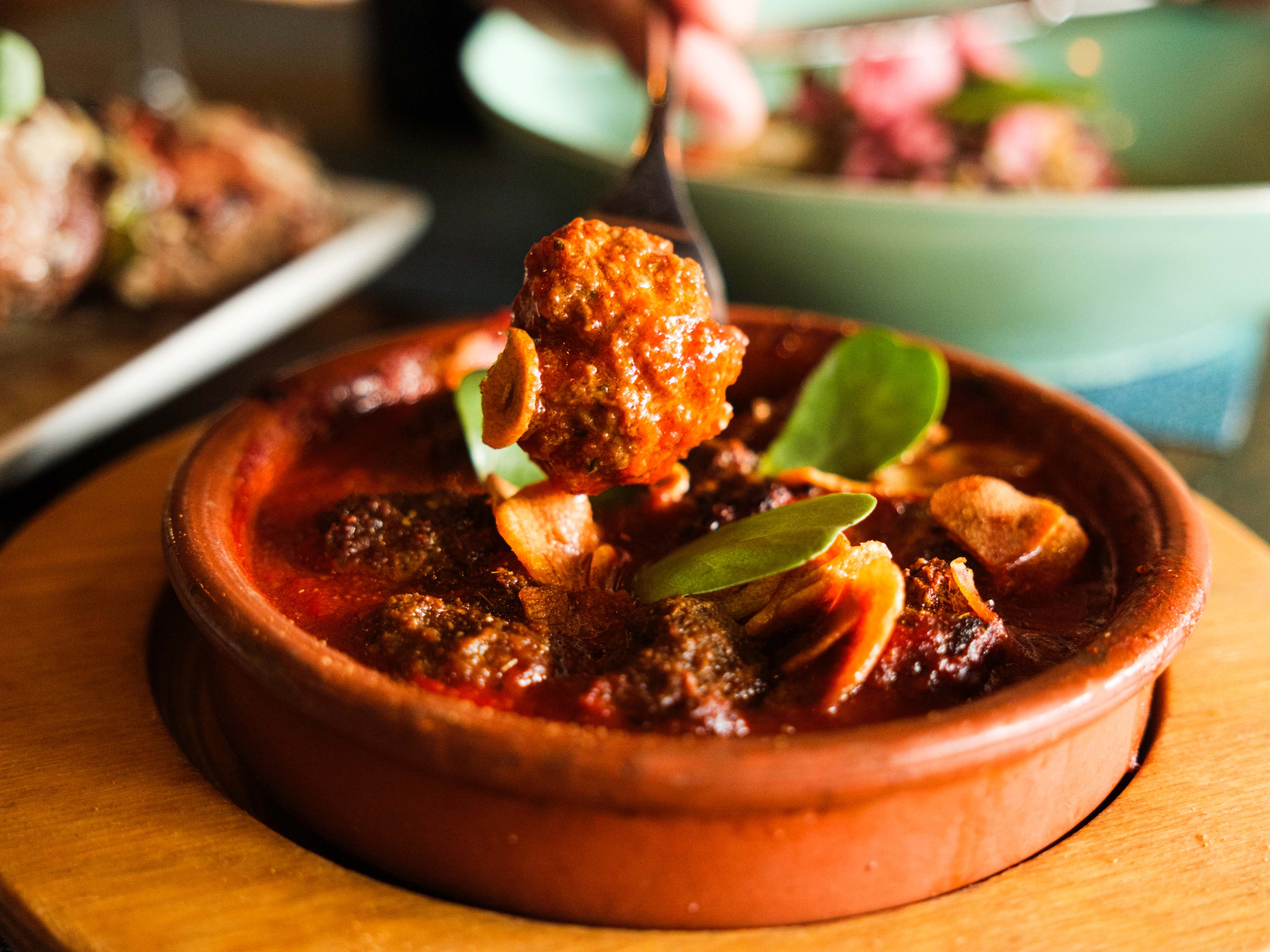 terracotta ramekin full of red sauce and small meatballs with slices of garlic