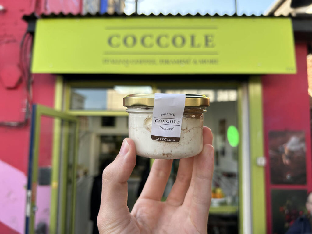 a pot of tiramisu being held up in front of a green shop called 'coccole'