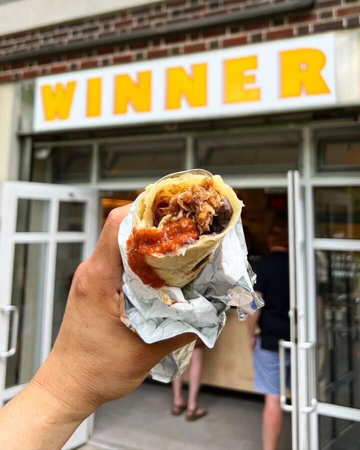 A hand holds up a burrito in front of Winner sign.