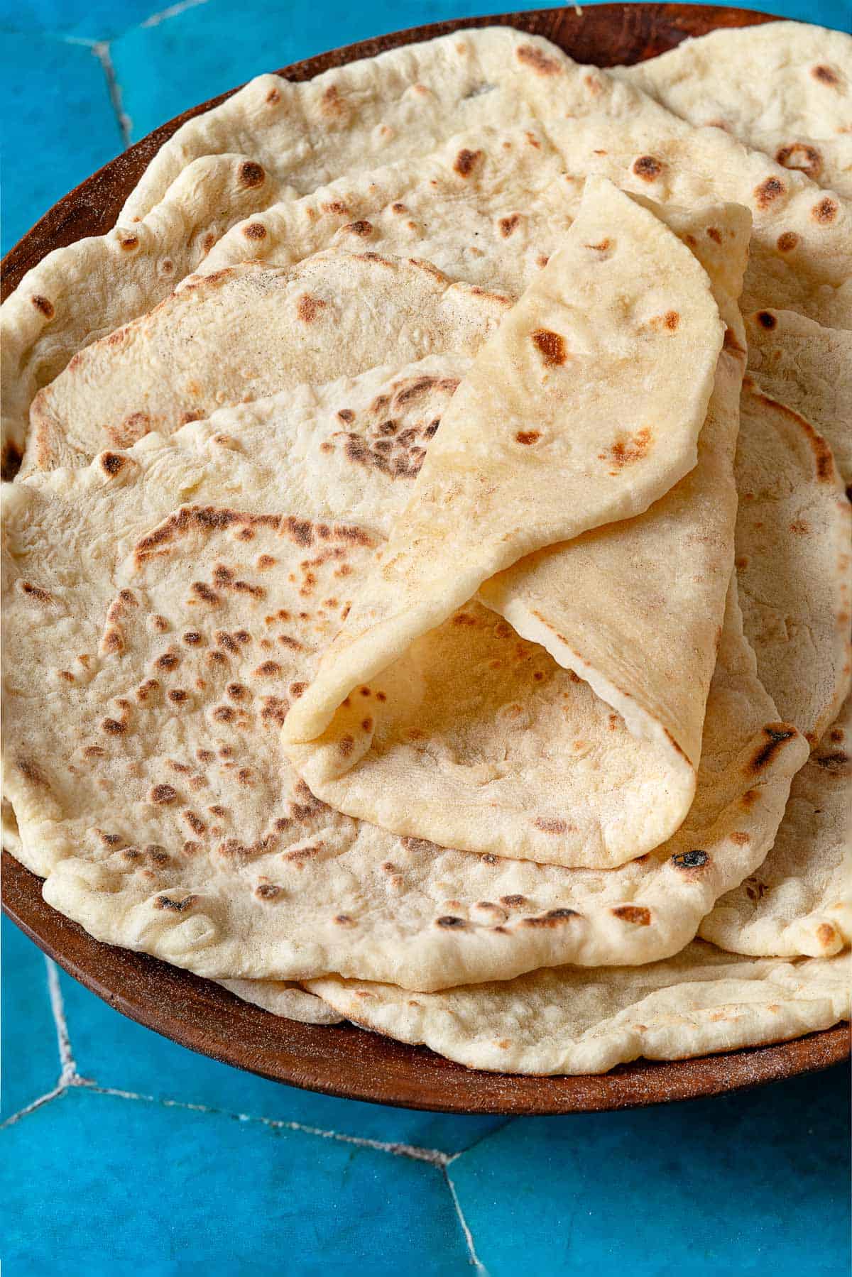 A stack of lavash bread in a wooden bowl. The top lavash is folded in a wrap shape, showing its flexibility.