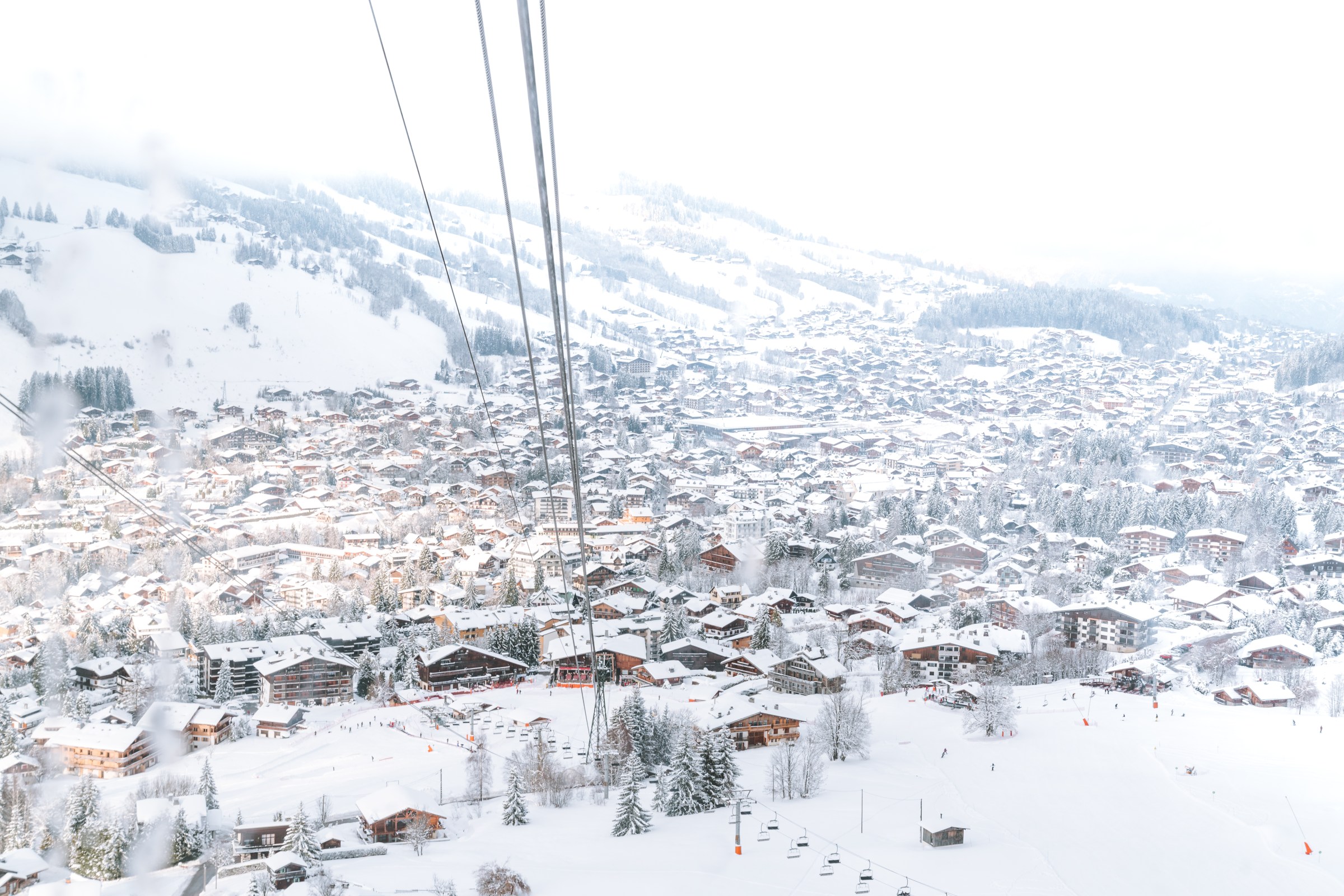 A snowy town, with wires running above for a ski lift and large mountains all around