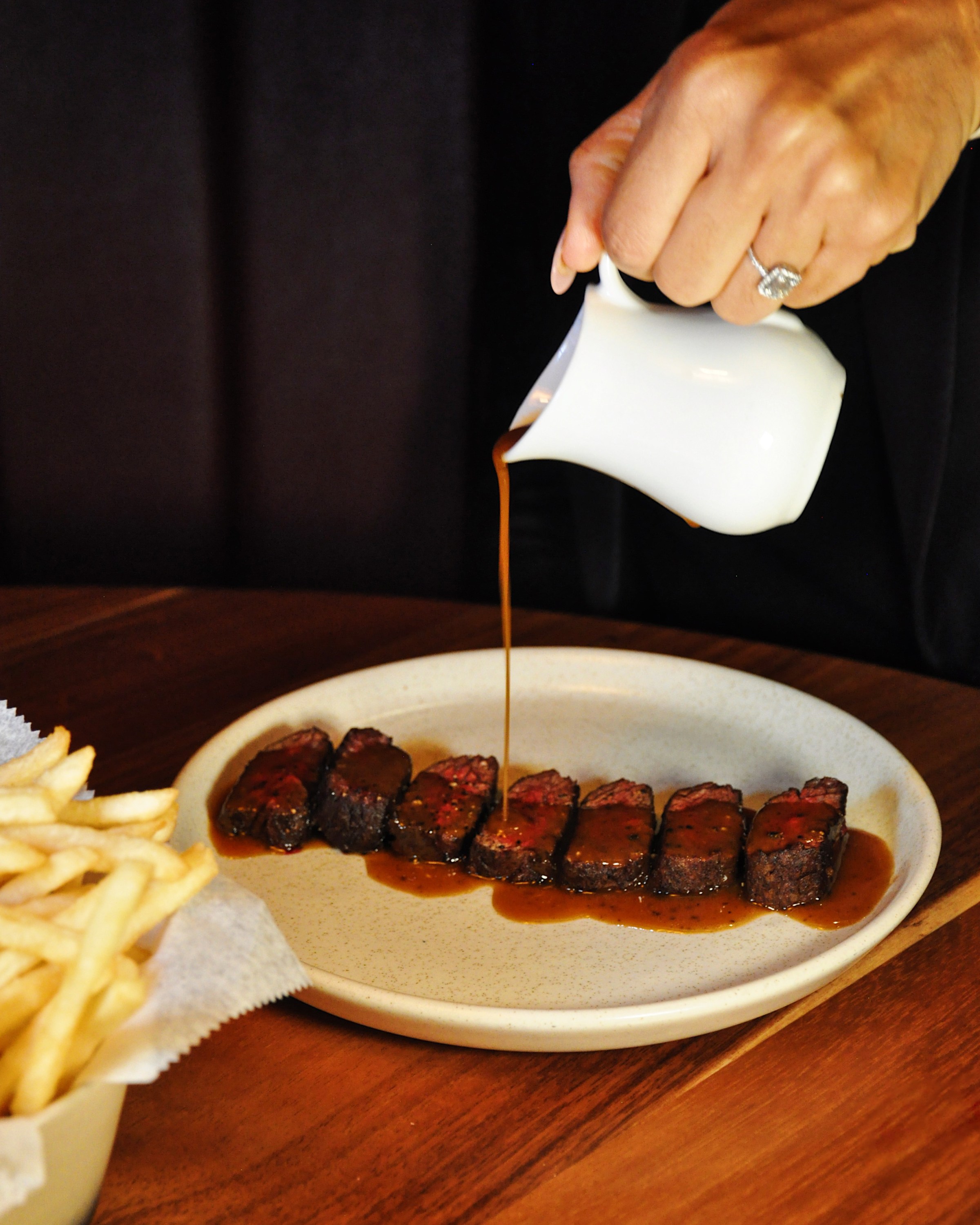 Pouring sauce over steak and fries.