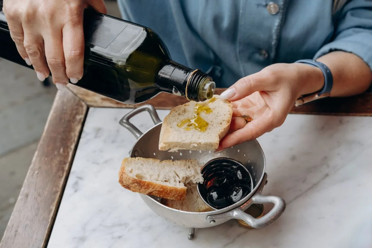 A woman's hands pour olive oil on a slice of bread.