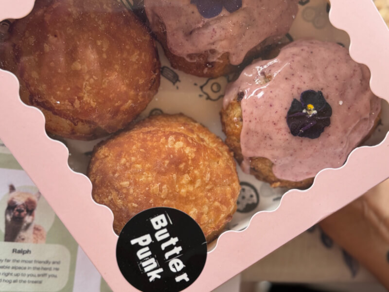 48 Hours in Asheville: A Culinary Tour Through an NC Gem - 7 A box of four pastries—two plain, two with pink icing and flower decorations—labeled "Butter Punk," channels the creative flair often found at Asheville restaurants. A leaflet featuring an alpaca photo is partially visible.