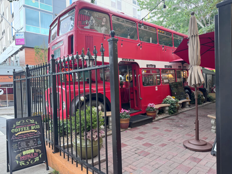 48 Hours in Asheville: A Culinary Tour Through an NC Gem - 16 A red double-decker bus converted into a café, one of the most unique Asheville restaurants, sits behind a black fence on a brick patio with potted plants and an outdoor sign displaying the menu.