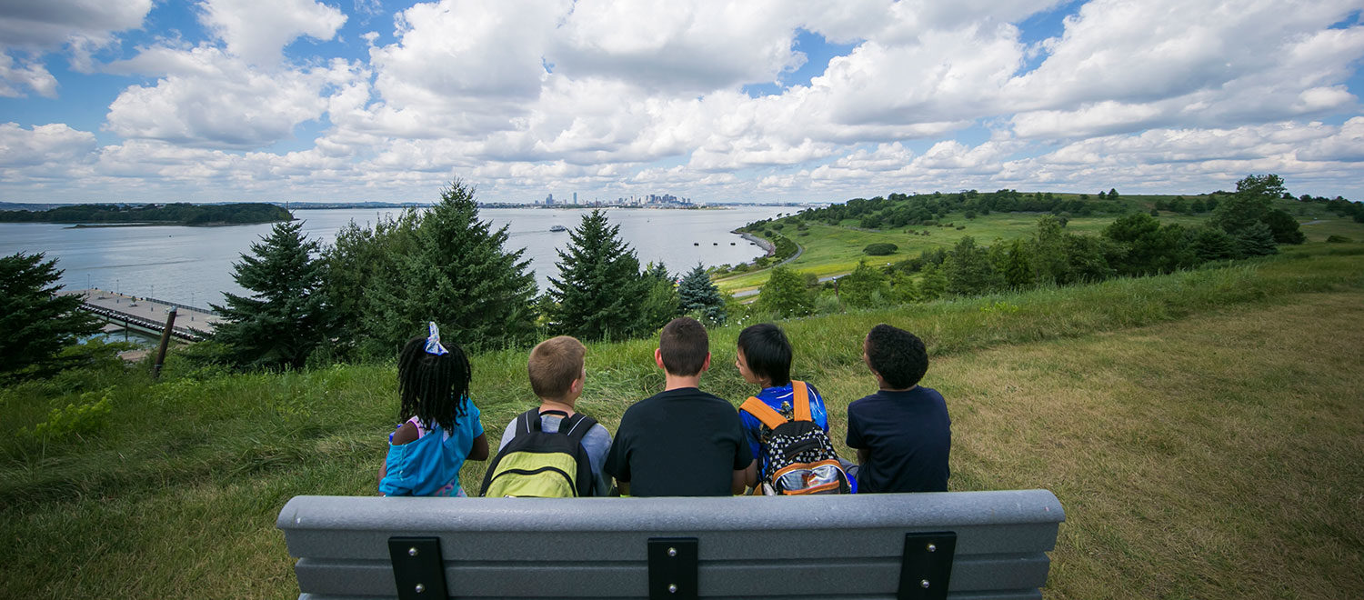 Five children sit on a bench on Spectacle Island looking off towards the Boston skyline