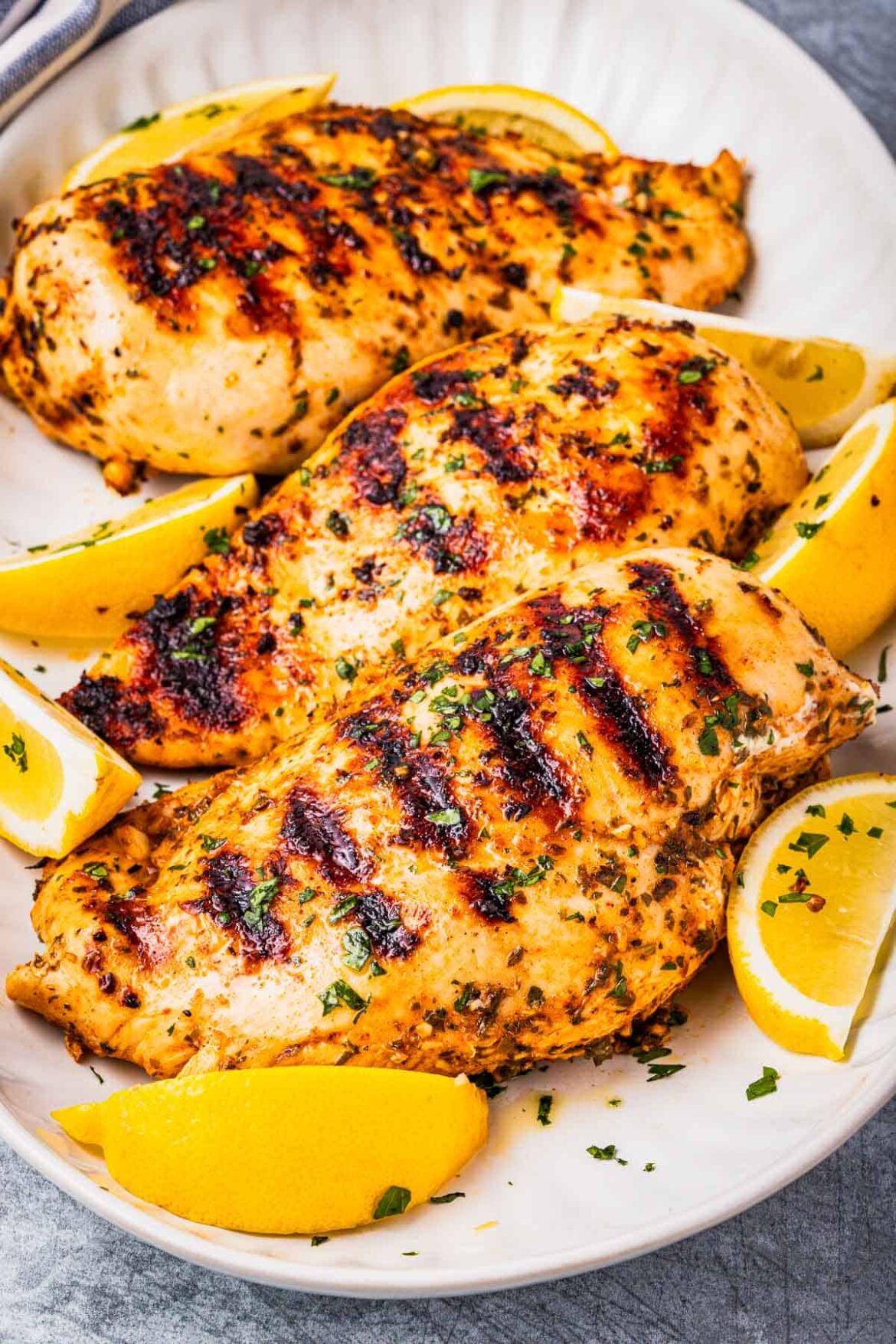 Marinade Recipes | The Mediterranean Dish Three grilled chicken breasts that have been marinated in Greek chicken marinade and are on a platter with lemon wedges and a sprinkle of parsley.