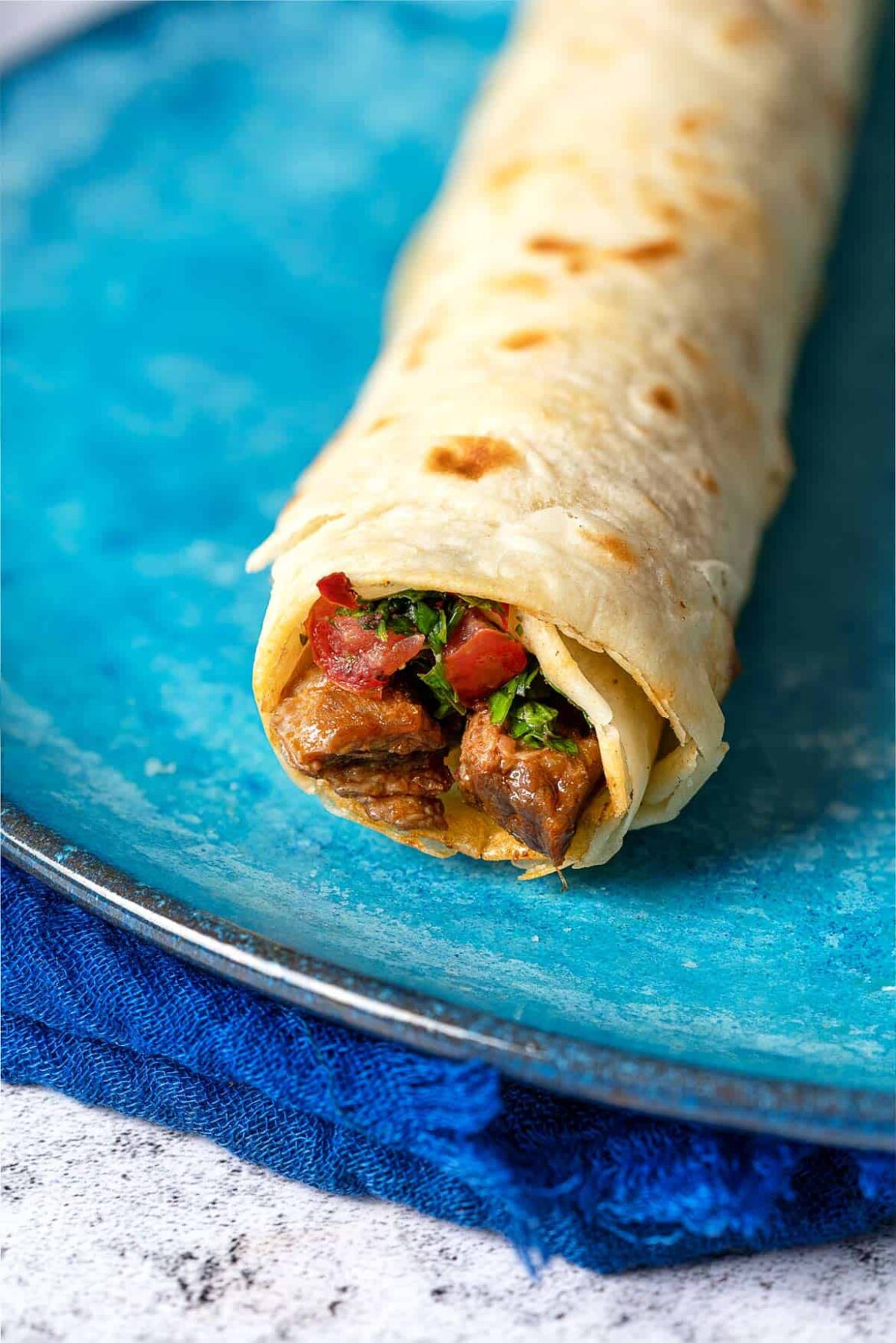 Tantuni (Turkish Steak Wraps) | The Mediterranean Dish Close of shot of a tantuni steak wrap that has been filled with steak and tomato salad.