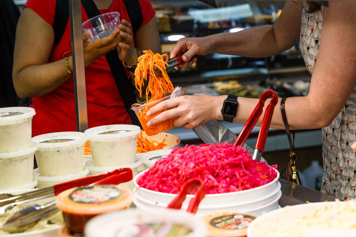 A patron uses tongs to place orange carrot kimchi into a takeout container