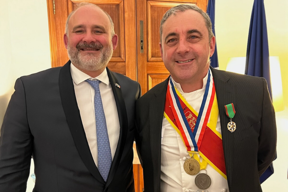 Two men in suits stand side by side, one is wearing medals. 