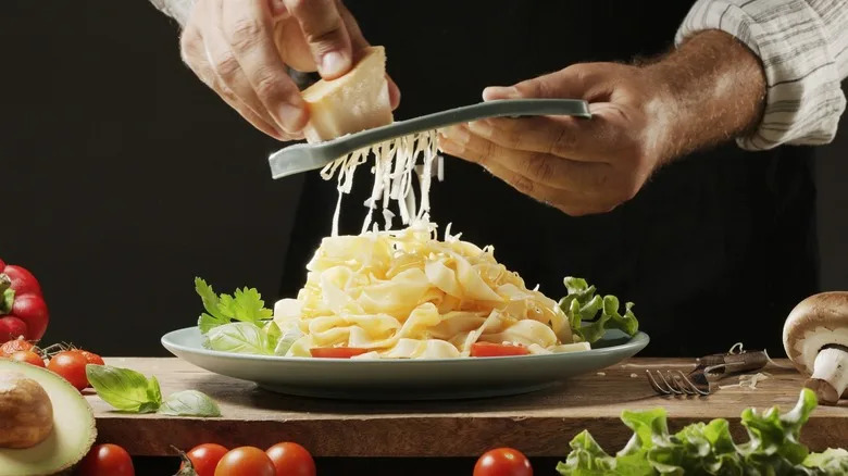 A chef grates cheese onto a pasta dish