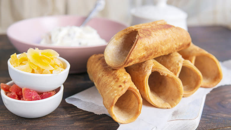 Cannoli shell in a pile beside a bowl of filling and bowls of toppings
