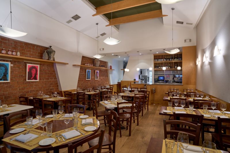 Angelini Osteria dining room with exposed brick walls and wooden tables set for service.