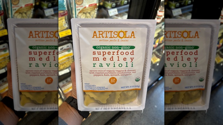 Hand holding a white box of ravioli pasta