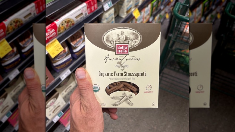 Hand holding a brown and beige box of farro strozzapreti pasta