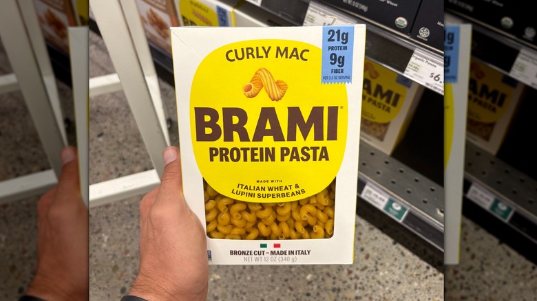 Hand holding a white, yellow, and blue box of curly mac protein pasta