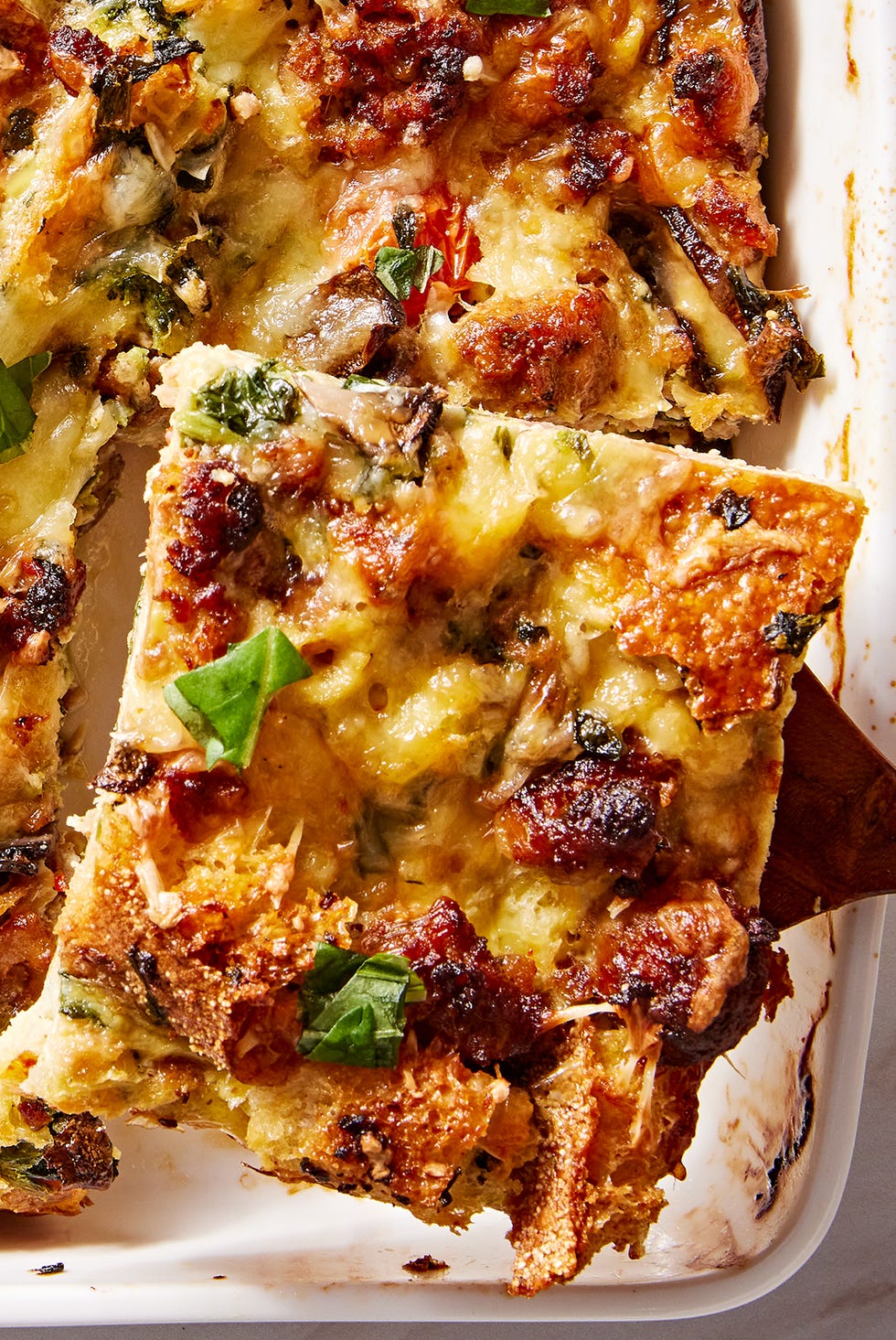 breakfast casserole in a white baking dish with italian sausage, mushrooms, tomatoes, and spinach