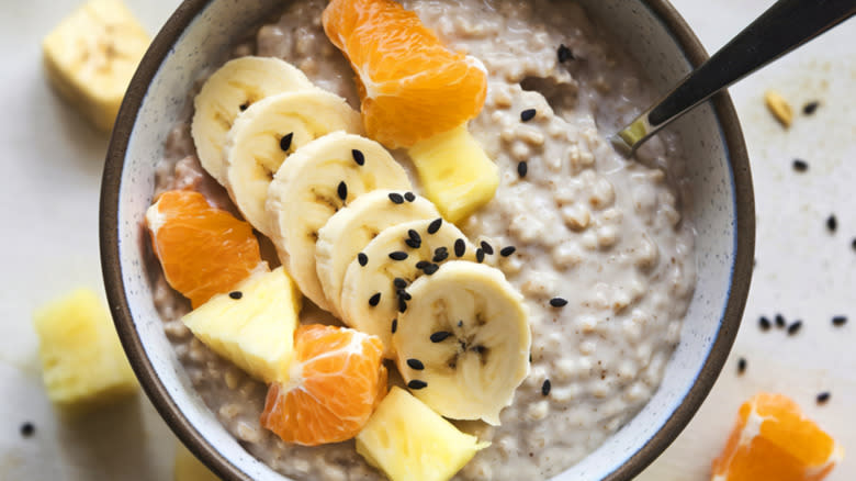 Bowl of creamy oatmeal with bananas, oranges, and pineapple,