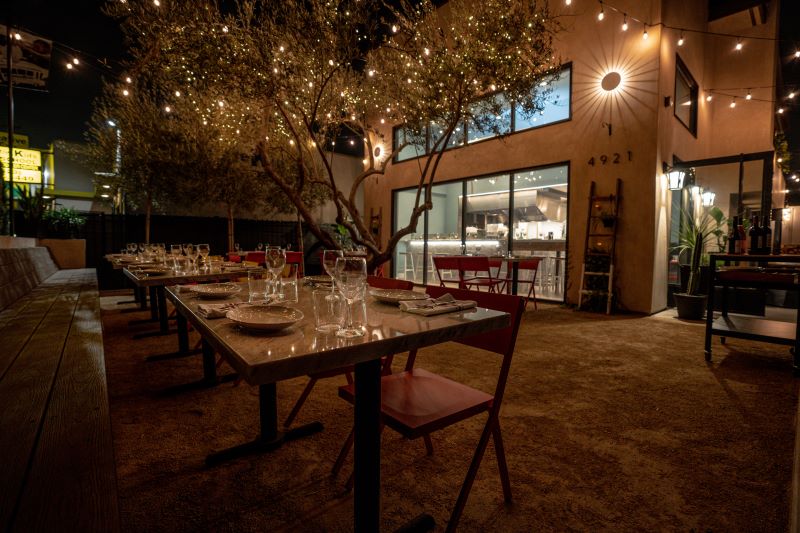Patio dining at cento with a table set for service beneath a tree decorated with string lights.