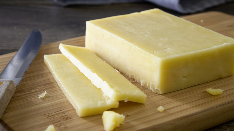 Block of cheddar cheese sliced on cutting board