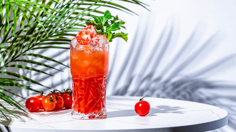 Tomato drink with cherry tomatoes on table by palm leaves