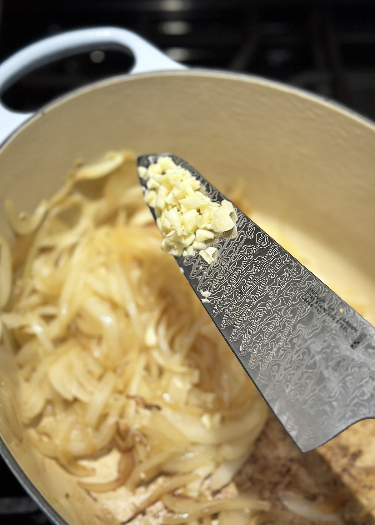 chopped garlic on knife blade over onion soup pot
