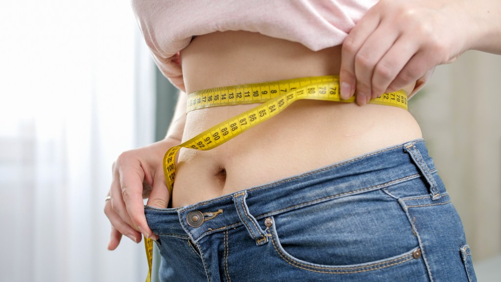 Woman measuring her waist with a tape measure.