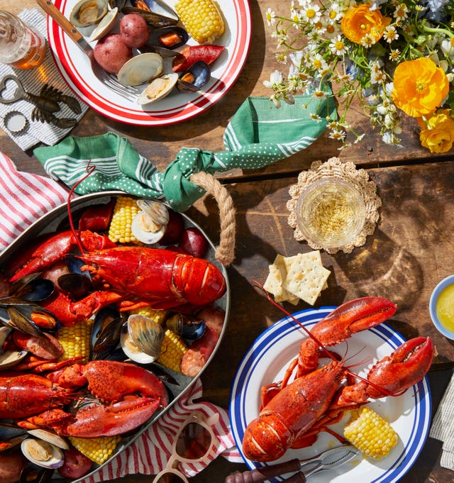 a lobster boil with clams potatoes and corn divided between red and white plates and a metal serving platter