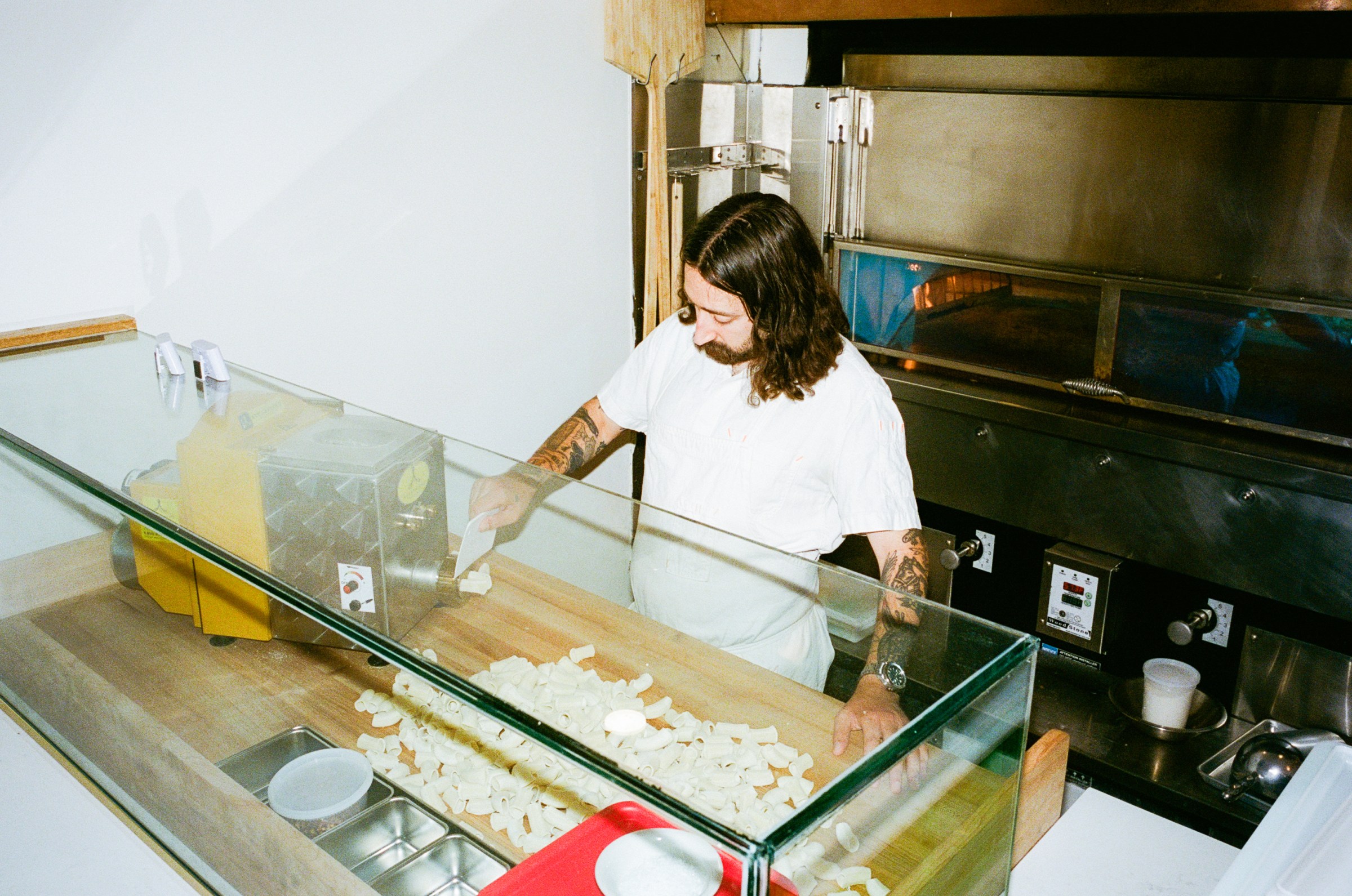 Chef Jack Goode behind the counter slicing pasta coming out of a machine
