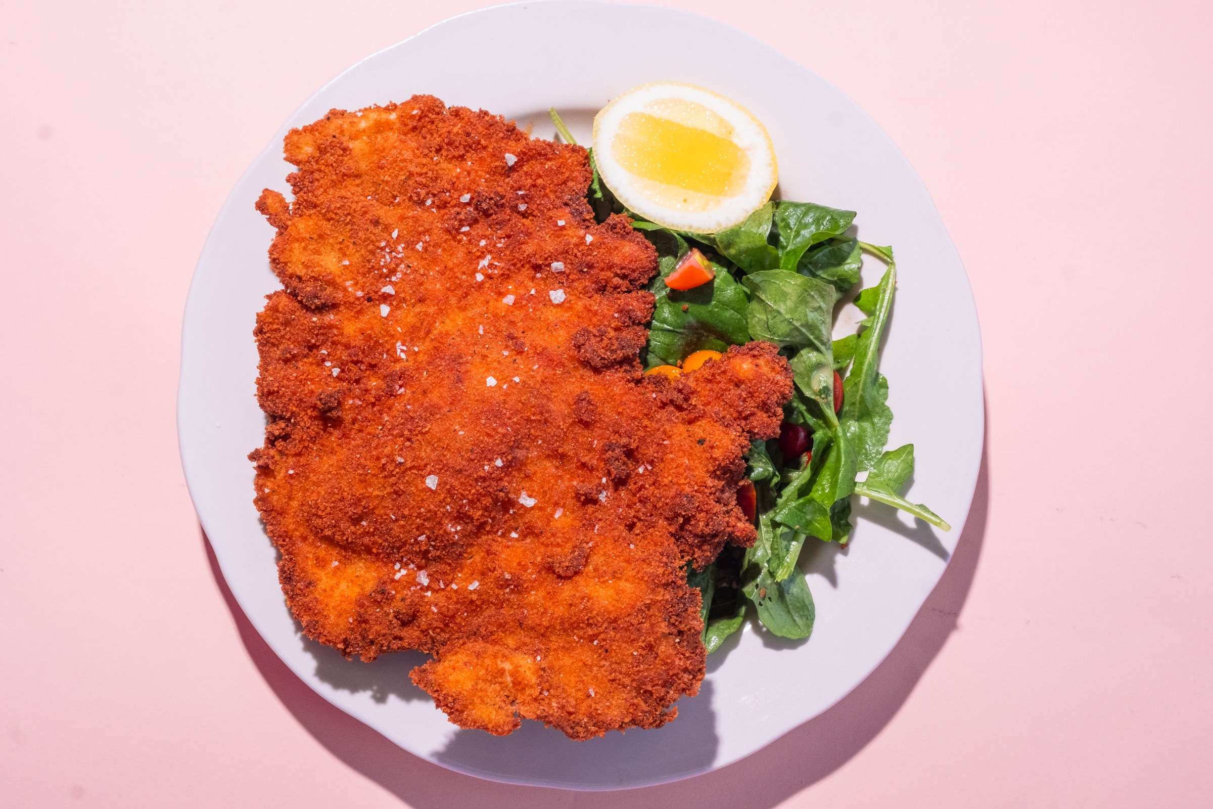 Overhead shot of Chicken Milanese with a side salad on a white plate against a pink back drop