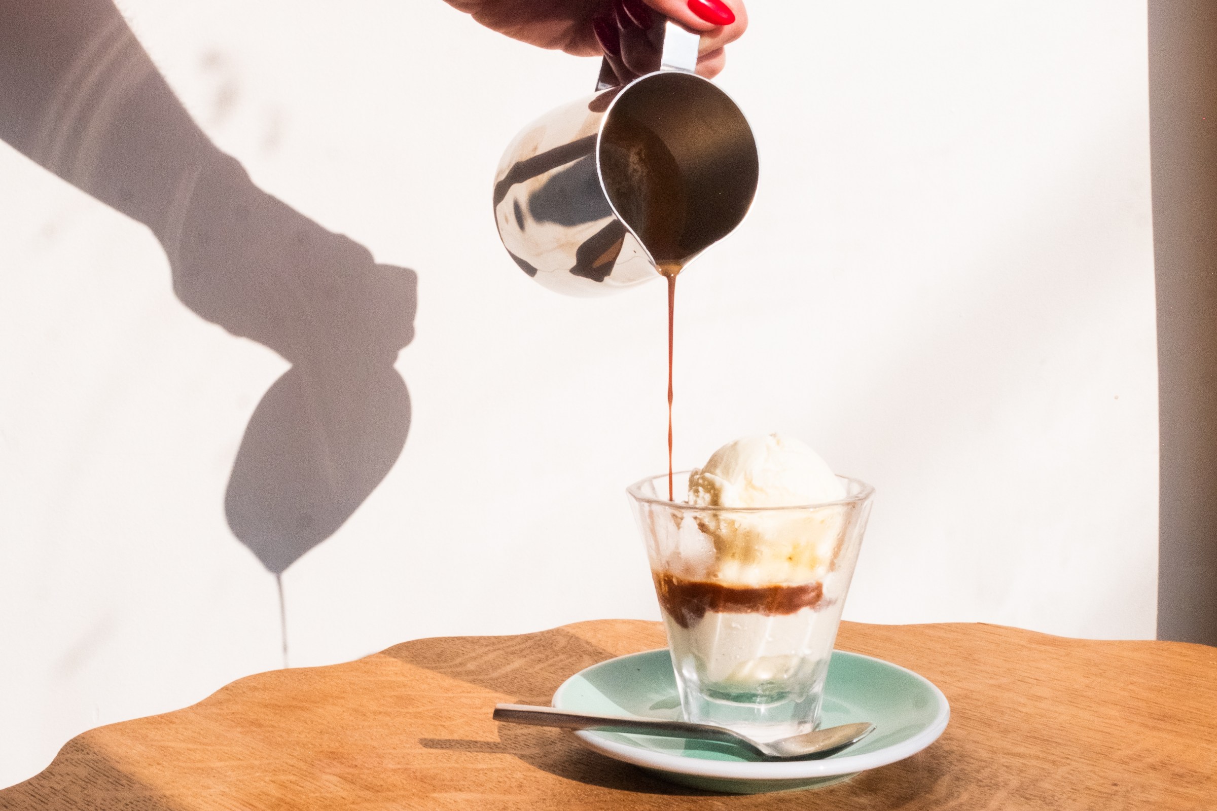 Hand pouring espresso over ice cream in a clear cup.