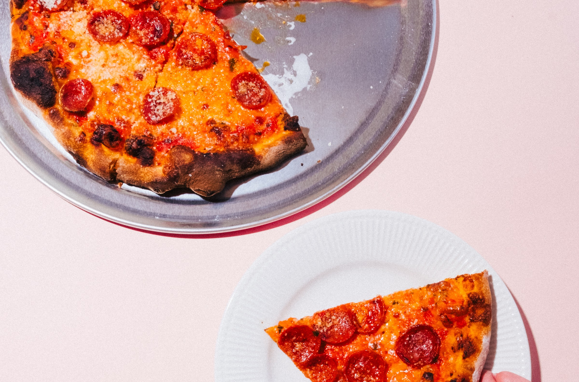 Hand holding a slice of pepperoni pizza with a full pie in the background at Companion