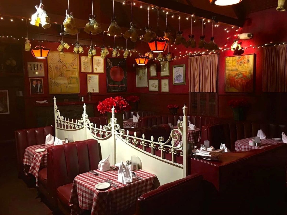 Tables in a retro dining room with red checkered table cloths and bottles hanging from the ceiling.