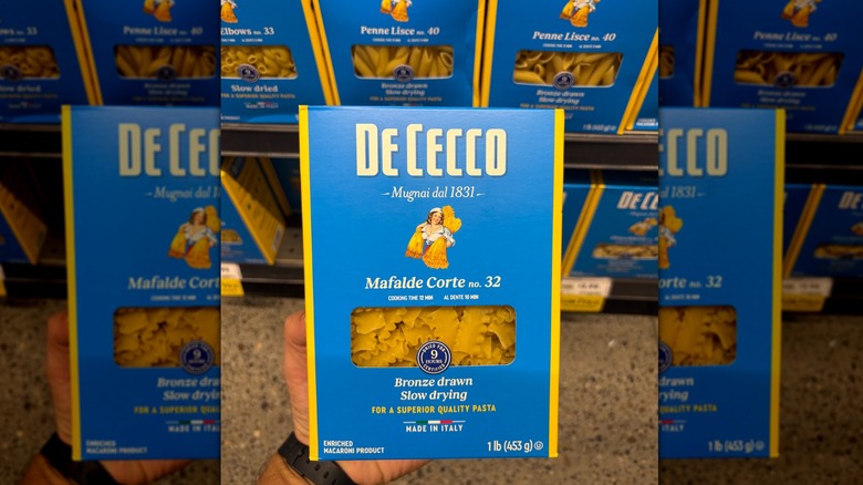 Hand holding a blue and yellow box of mafalde corte pasta