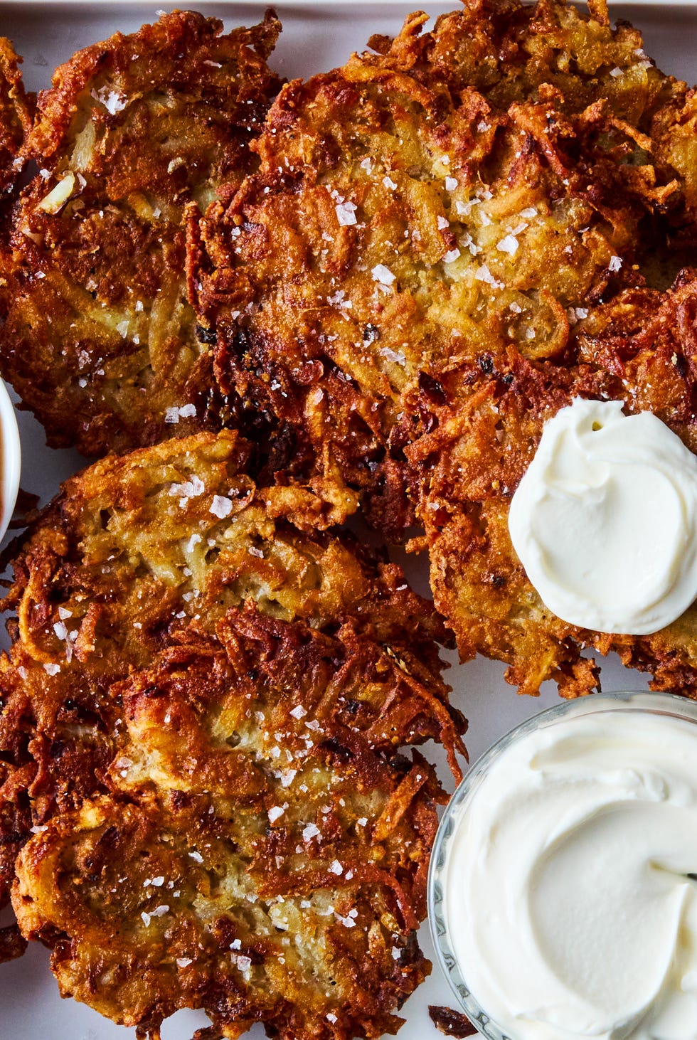 crispy latkes on a platter with bowls of sour cream and applesauce