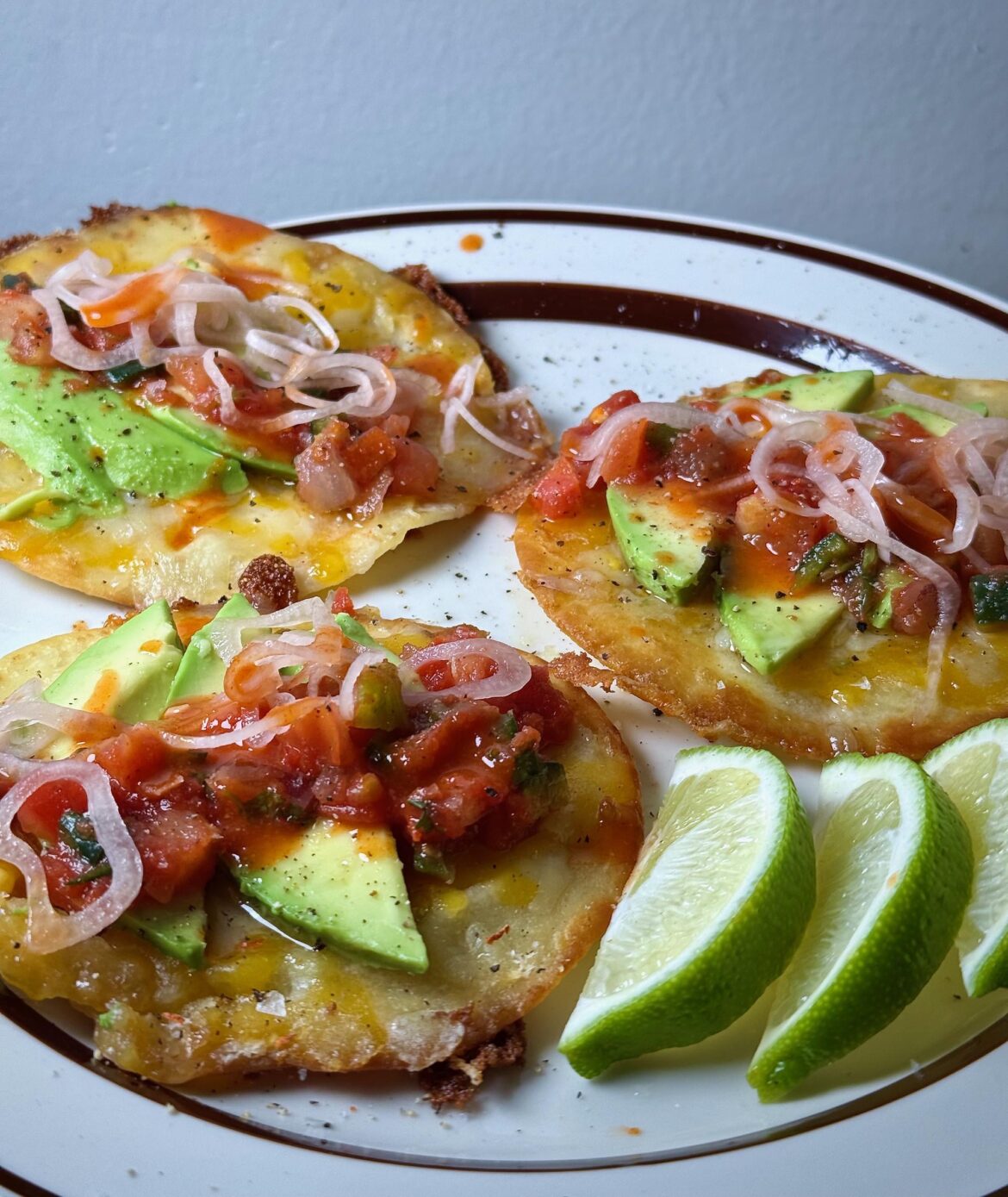 Tostadas de queso con salsa, rodajas de aguacate, cebolla encurtida y un toque de Valentina.