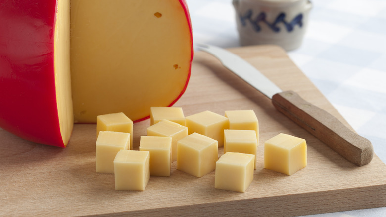 Cubes cut from wheel of Edam cheese on wooden cutting board