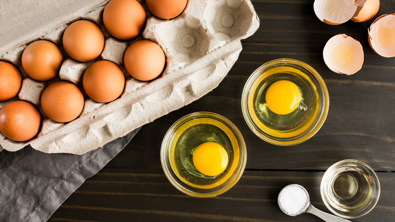 Egg carton by two cups of cracked raw eggs