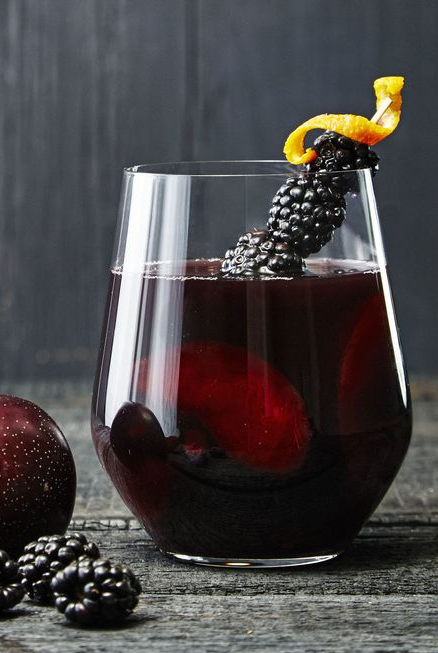 a glass of blackberry punch with blackberry garnish on a dark table