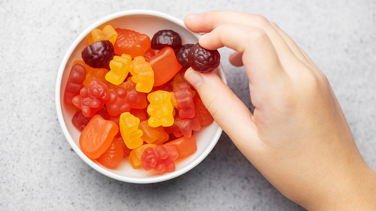 hand holds a gummy vitamin over a bowl
