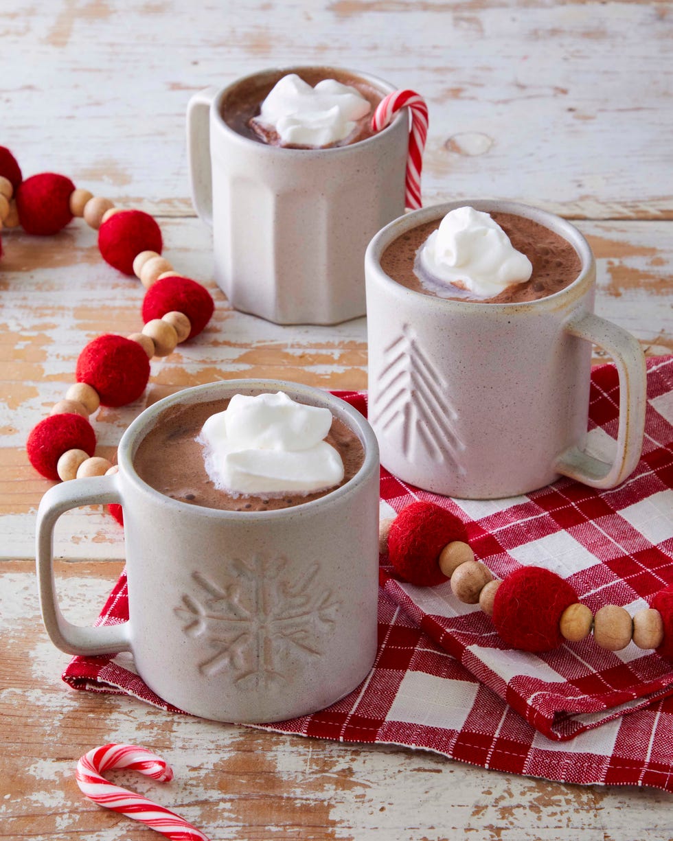 hot chocolate in ceramic mugs topped with whipped cream on a red and white dishtowel