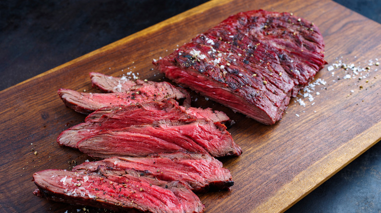 A sliced, medium-rare grilled bavette steak surrounded by ground pepper on a cutting board