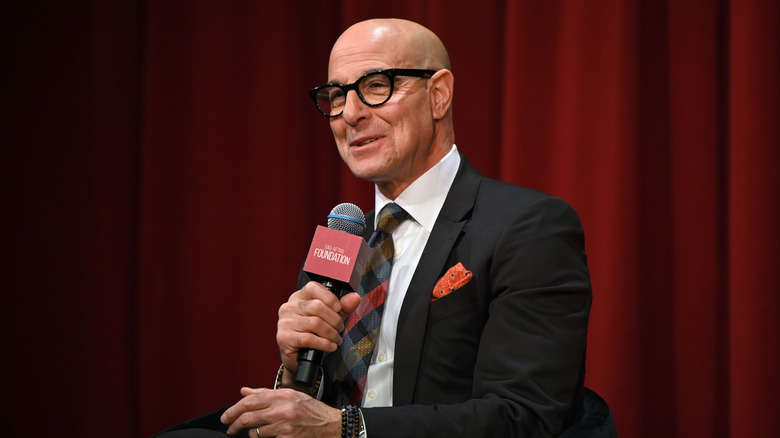 Stanley Tucci smiling and laughing holding microphone