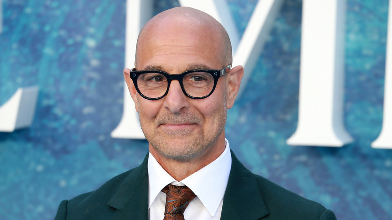 Stanley Tucci smiling in green suit and red tie