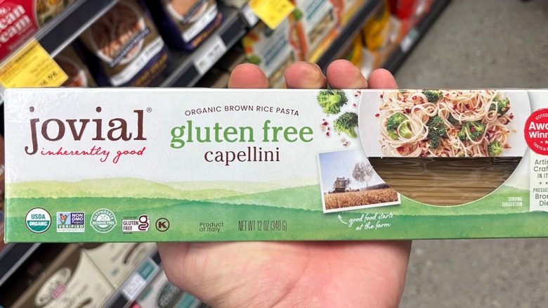 Hand holding a white and green box of capellini pasta