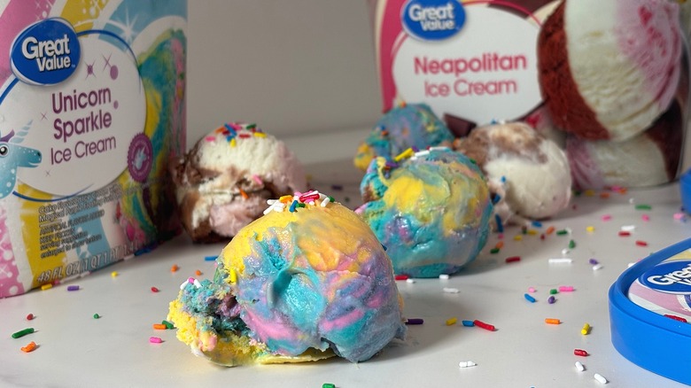 Scoops of Neapolitan and Unicorn Sparkle ice creams in front of tubs with sprinkles on white table