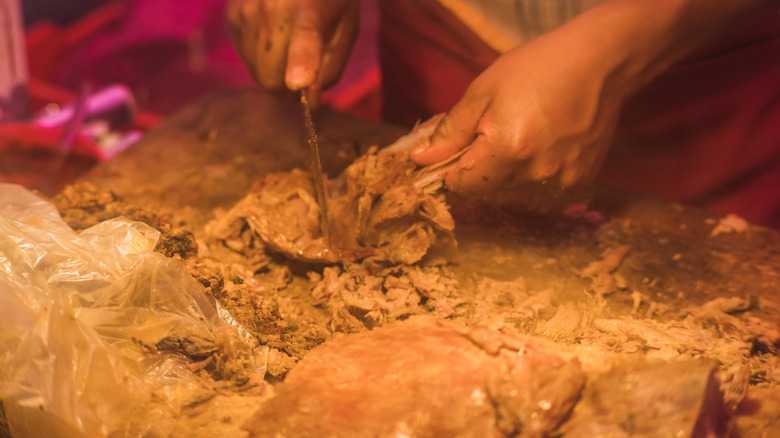 Lamb barbacoa being cut on a chopping board at a Mexican market stall