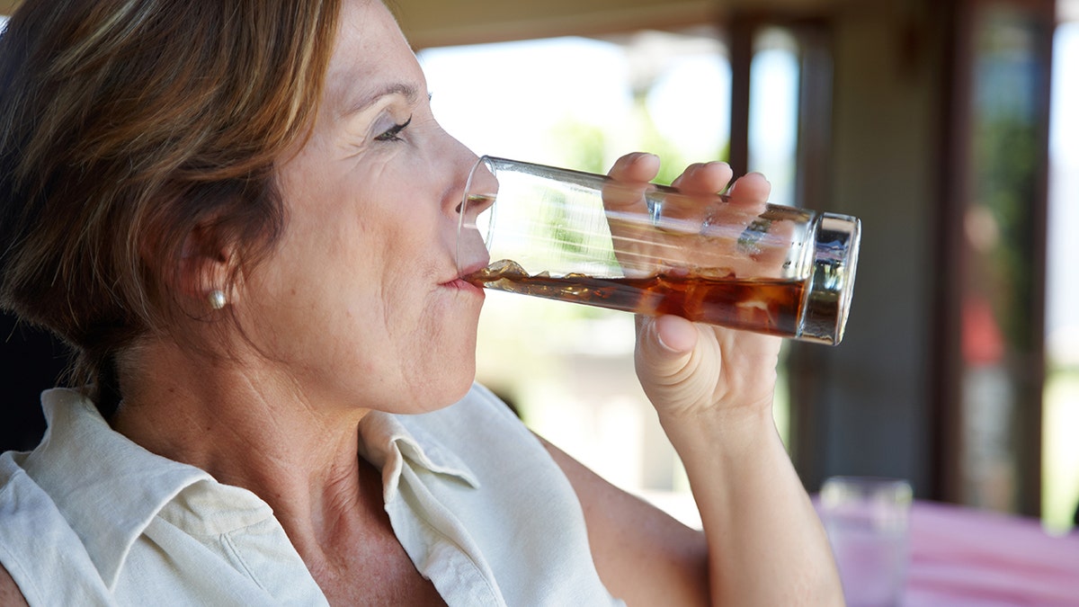 An older woman is drinking a soda from a glass.