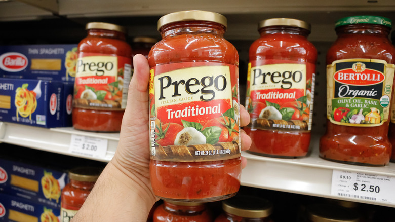 A person holding a jar of Prego Traditional Italian Sauce in a grocery store