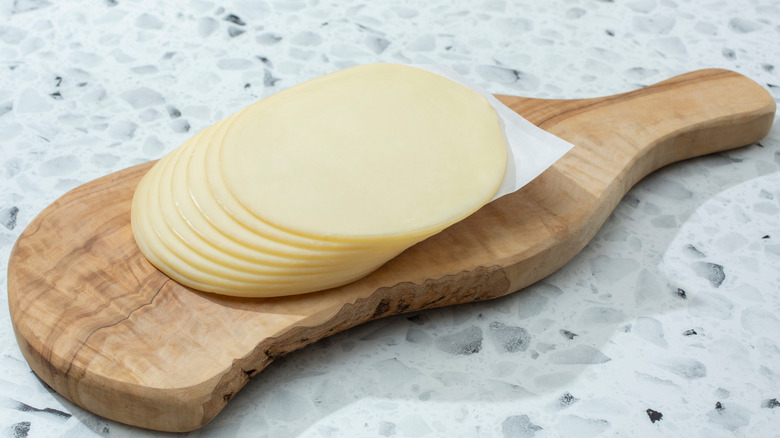 Stack of sliced provolone cheese on wooden cutting board